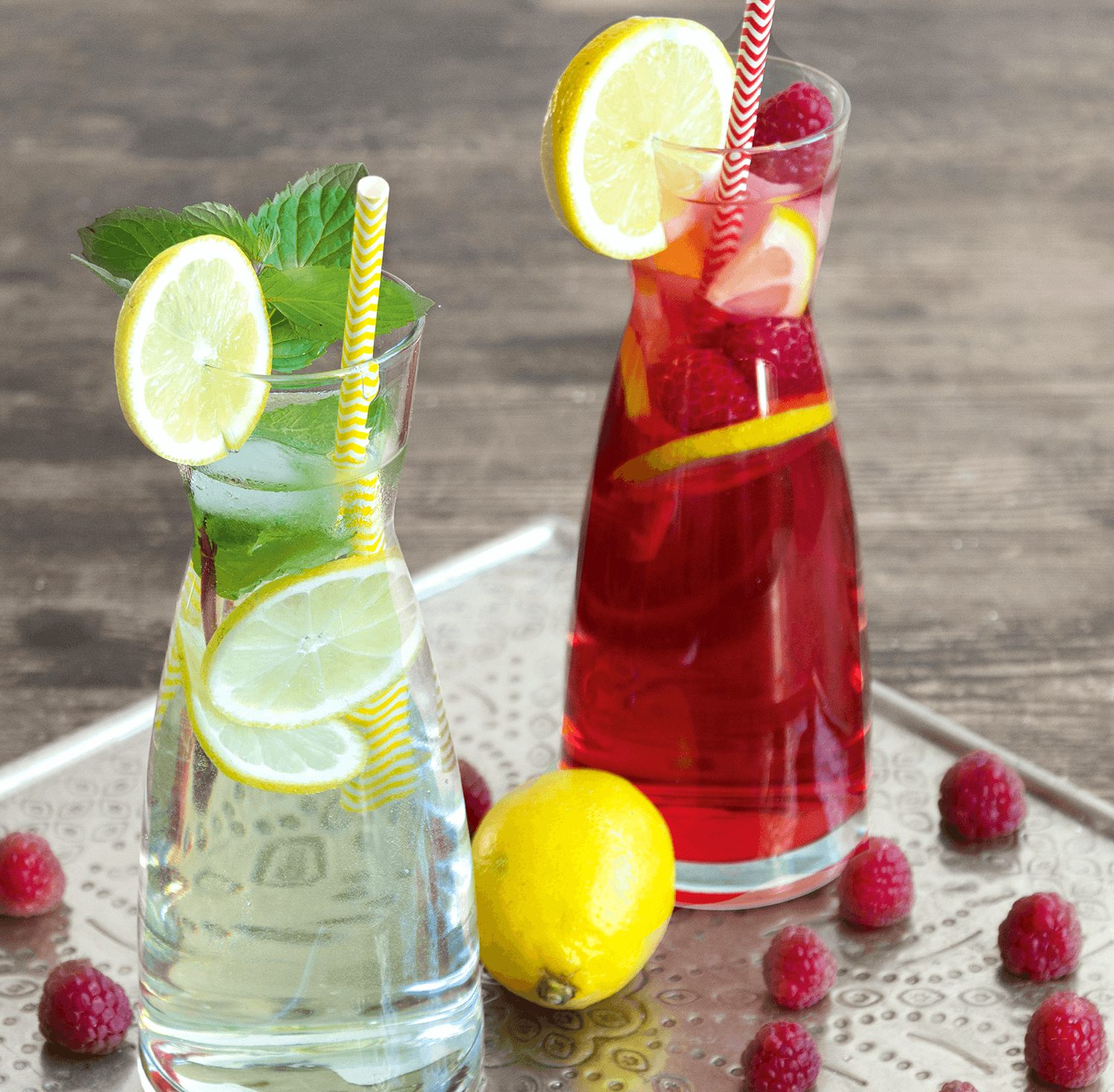 Karaffen gefüllt mit Himbeer- und Holunderblütensirup mit Minze, Himbeeren und Zitronen garniert auf einem silber Tablett.